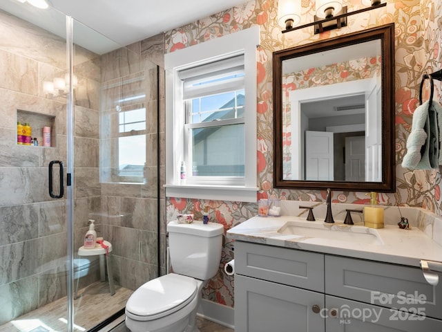 bathroom featuring wallpapered walls, vanity, a shower stall, and toilet