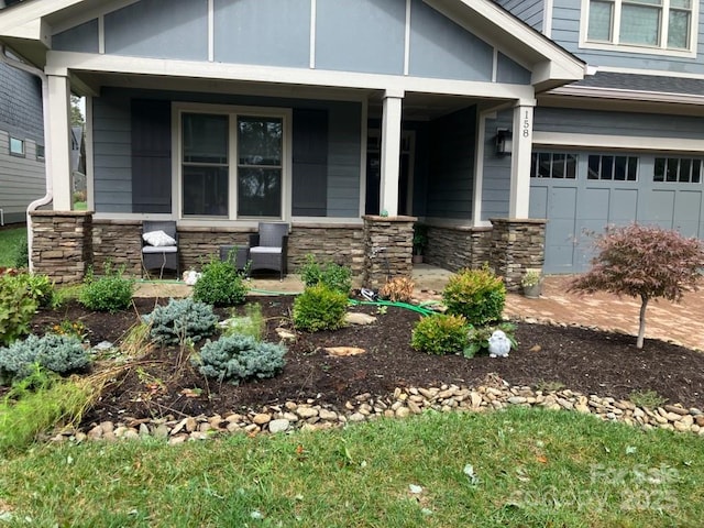 view of front of property featuring covered porch, stone siding, and an attached garage