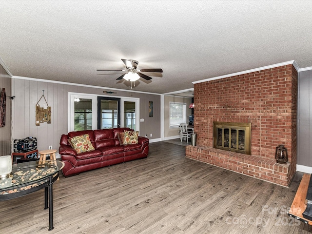 living room featuring crown molding, a textured ceiling, a ceiling fan, wood finished floors, and a brick fireplace