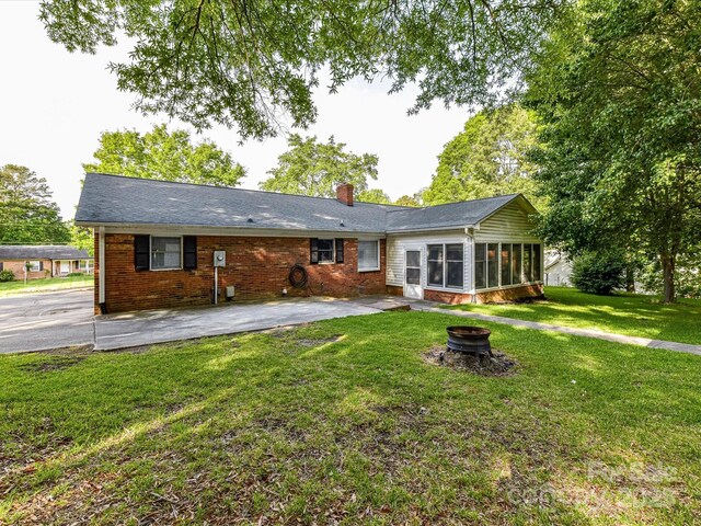 rear view of house featuring a sunroom, an outdoor fire pit, a chimney, a patio, and a yard