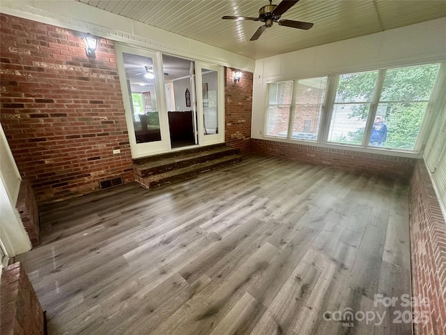 unfurnished sunroom featuring brick wall and wood finished floors