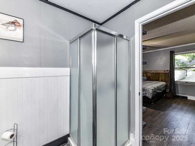 ensuite bathroom with a wainscoted wall, wood finished floors, a shower stall, and wood walls