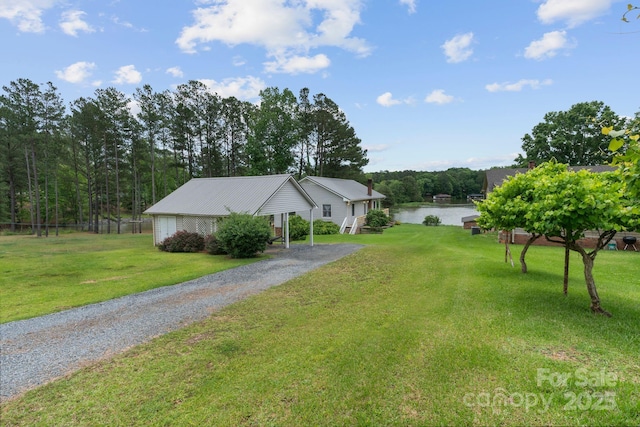 view of grassy yard featuring gravel driveway and a water view
