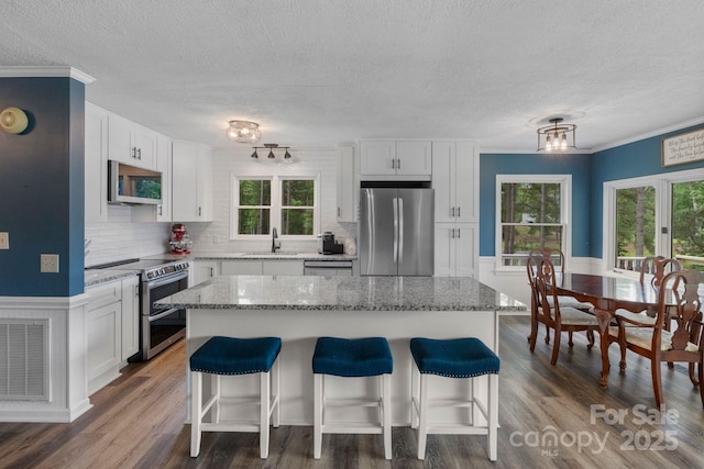 kitchen featuring appliances with stainless steel finishes, a sink, a textured ceiling, a kitchen bar, and white cabinetry