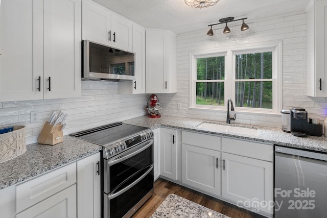 kitchen featuring appliances with stainless steel finishes, a sink, white cabinets, dark wood-type flooring, and backsplash