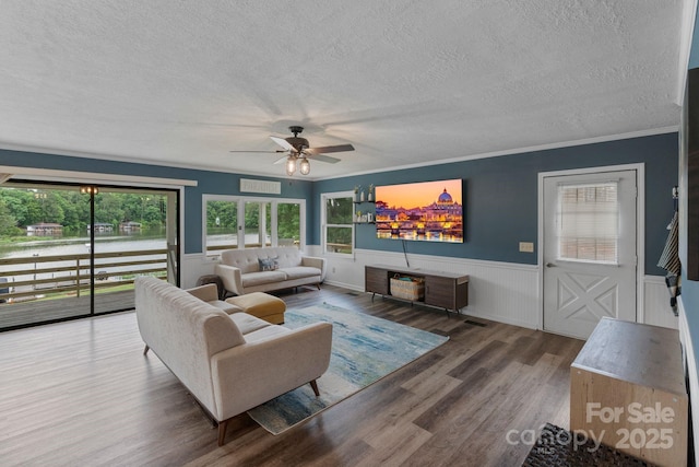 living room with a textured ceiling, a ceiling fan, wood finished floors, wainscoting, and crown molding