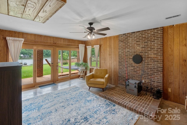 sitting room featuring wood walls, healthy amount of natural light, a ceiling fan, a water view, and a wood stove