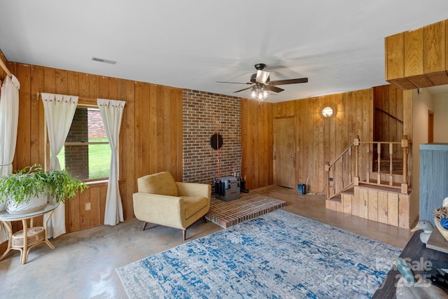 living area with wooden walls, a wood stove, ceiling fan, and stairs