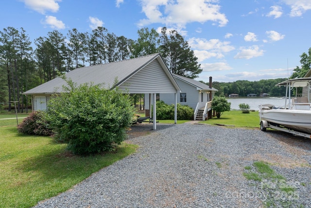 view of home's exterior featuring gravel driveway, a lawn, metal roof, a detached carport, and a water view