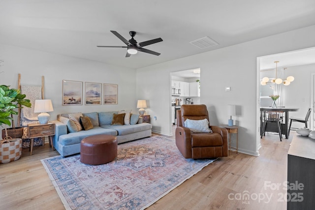 living room featuring visible vents, light wood-style flooring, ceiling fan with notable chandelier, and baseboards