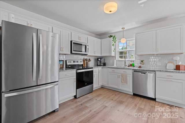 kitchen with light wood-style floors, appliances with stainless steel finishes, decorative backsplash, and white cabinetry