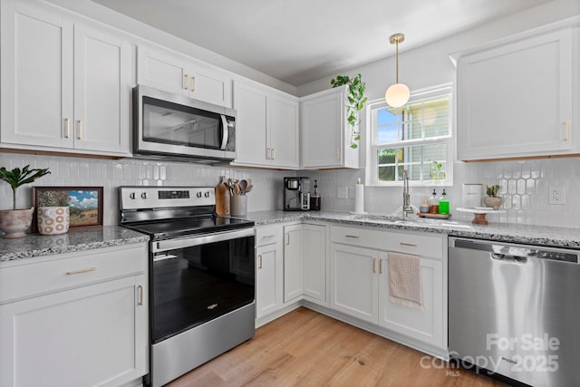 kitchen with decorative backsplash, white cabinetry, a sink, light wood-style flooring, and appliances with stainless steel finishes