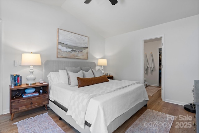 bedroom featuring ceiling fan, vaulted ceiling, wood finished floors, baseboards, and ensuite bath