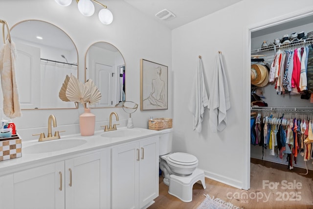 bathroom featuring double vanity, visible vents, a sink, and wood finished floors