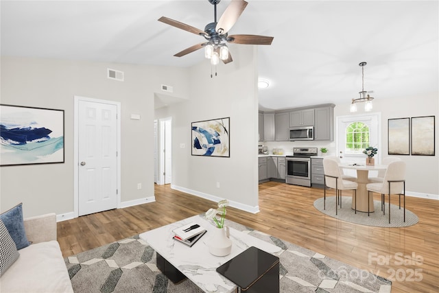 living room with baseboards, visible vents, lofted ceiling, and light wood-style floors