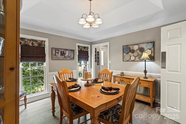 dining area with a wainscoted wall, light wood-type flooring, crown molding, and a notable chandelier