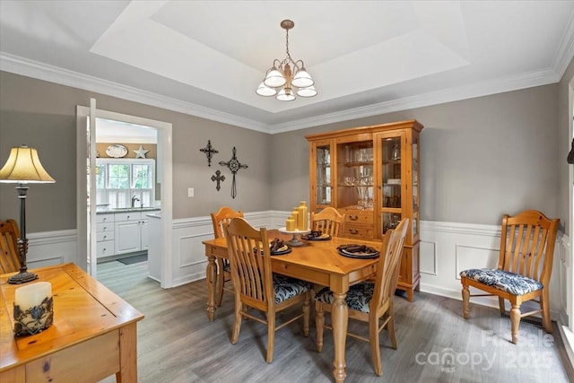 dining area featuring an inviting chandelier, wood finished floors, wainscoting, and a raised ceiling