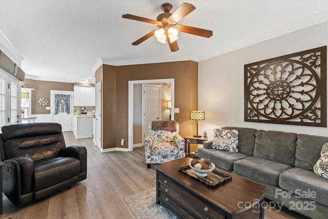 living room featuring crown molding, baseboards, a ceiling fan, and light wood finished floors
