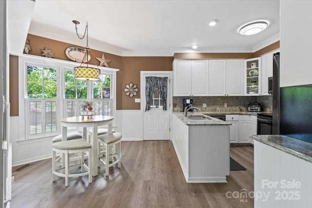 kitchen featuring electric range oven, wainscoting, a peninsula, wood finished floors, and white cabinets