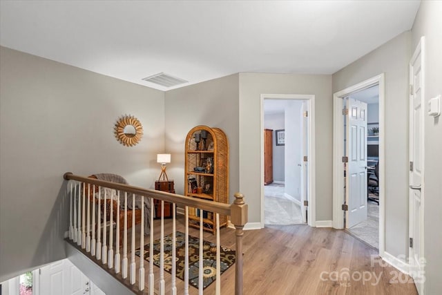 hallway with baseboards, light wood-style floors, an upstairs landing, and visible vents