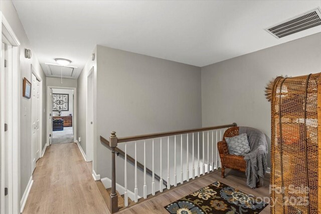 hallway featuring attic access, light wood-type flooring, an upstairs landing, visible vents, and baseboards