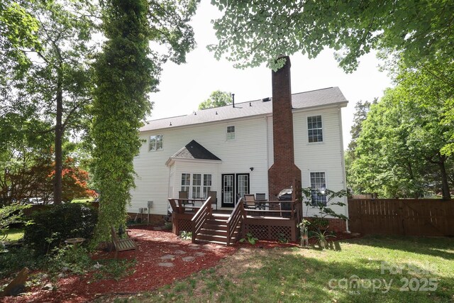 back of property with a lawn, a chimney, fence, and a deck
