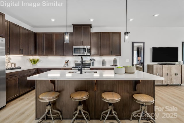 kitchen with backsplash, appliances with stainless steel finishes, a sink, and light wood-style flooring