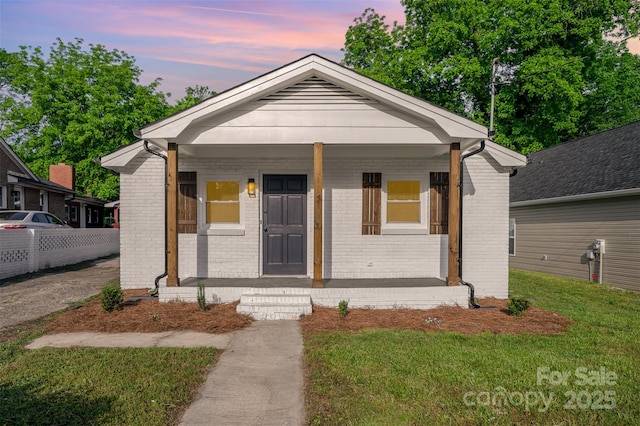bungalow featuring brick siding, a yard, and covered porch