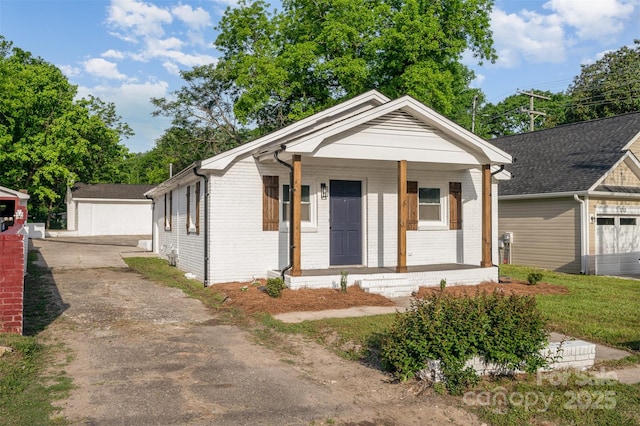 view of front facade featuring brick siding, an outbuilding, covered porch, and driveway