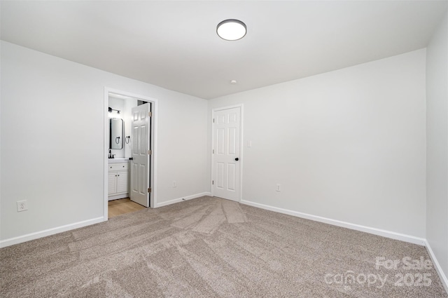 unfurnished bedroom with baseboards, ensuite bath, and light colored carpet