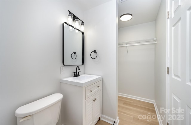 bathroom featuring a walk in closet, wood finished floors, vanity, baseboards, and toilet