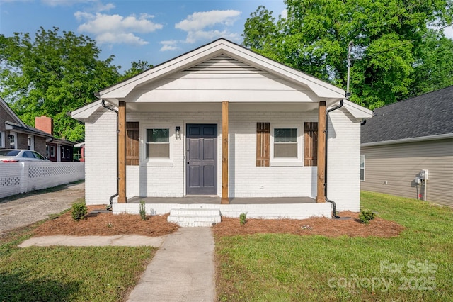 bungalow featuring covered porch, a front yard, and brick siding
