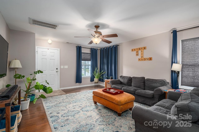 living room with visible vents, baseboards, ceiling fan, and dark wood-style floors