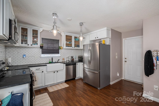 kitchen with dark countertops, appliances with stainless steel finishes, a sink, decorative backsplash, and dark wood-style floors