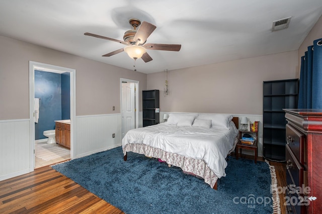 bedroom featuring connected bathroom, wainscoting, wood finished floors, and visible vents