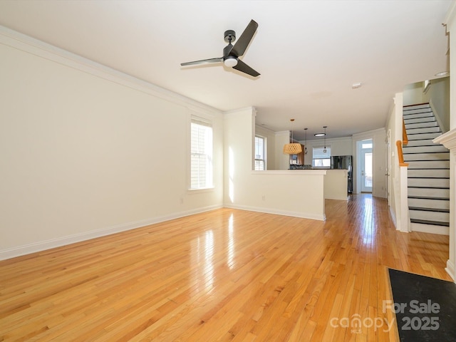 unfurnished living room featuring crown molding, light wood-type flooring, a ceiling fan, and stairs
