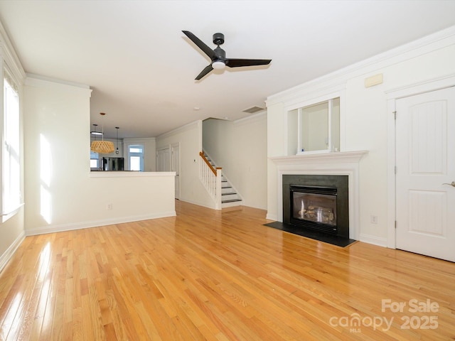 unfurnished living room featuring wood finished floors, a ceiling fan, a fireplace with flush hearth, stairway, and ornamental molding