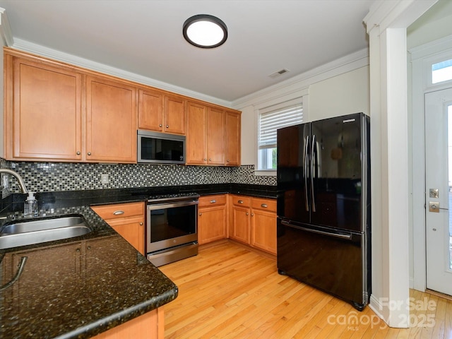 kitchen with a sink, tasteful backsplash, visible vents, light wood finished floors, and appliances with stainless steel finishes