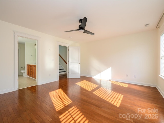 empty room featuring wood-type flooring, baseboards, a ceiling fan, and a wealth of natural light
