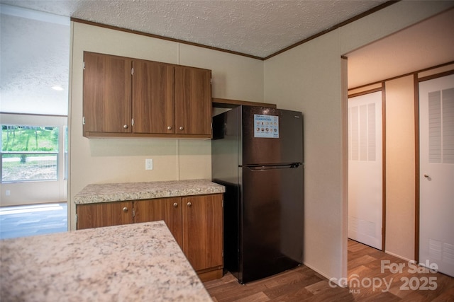 kitchen featuring freestanding refrigerator, light wood-type flooring, light countertops, a textured ceiling, and brown cabinets