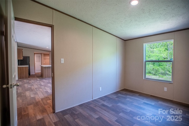 empty room with crown molding, a textured ceiling, vaulted ceiling, and wood finished floors
