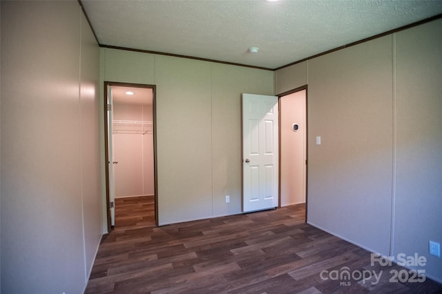 unfurnished bedroom with a walk in closet, a decorative wall, a textured ceiling, wood finished floors, and a closet