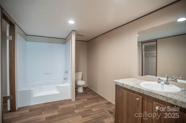 bathroom featuring vanity, visible vents, wood finished floors, toilet, and a washtub