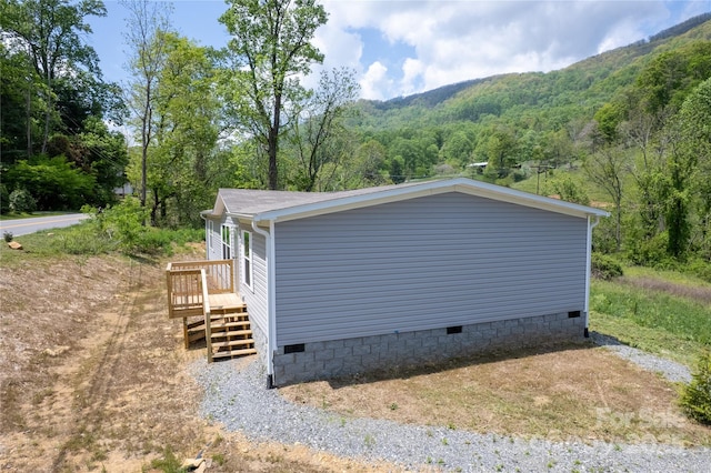 view of side of home featuring a wooded view, a deck with mountain view, stairway, and crawl space