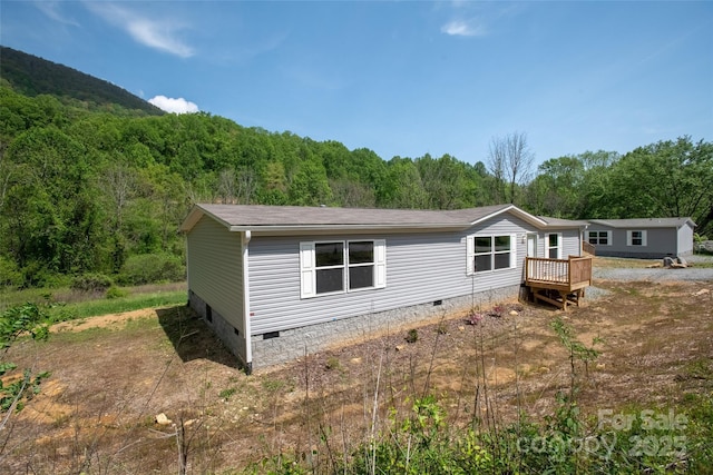 exterior space with a wooden deck, a forest view, a shingled roof, and crawl space
