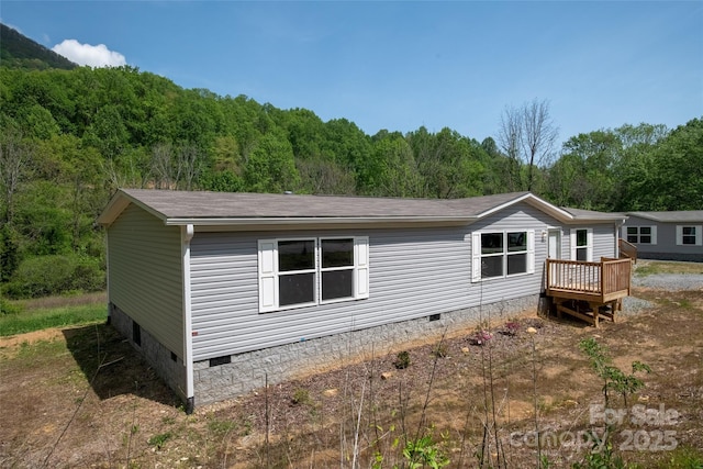 exterior space with a wooded view, a shingled roof, and crawl space