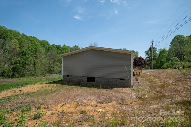 view of property exterior featuring crawl space, a forest view, and a deck