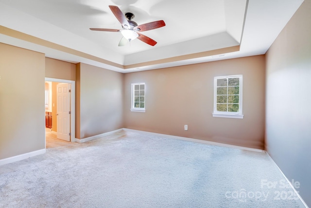 spare room featuring light colored carpet, a ceiling fan, a raised ceiling, and a healthy amount of sunlight
