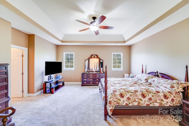 bedroom with carpet floors, a tray ceiling, multiple windows, and baseboards