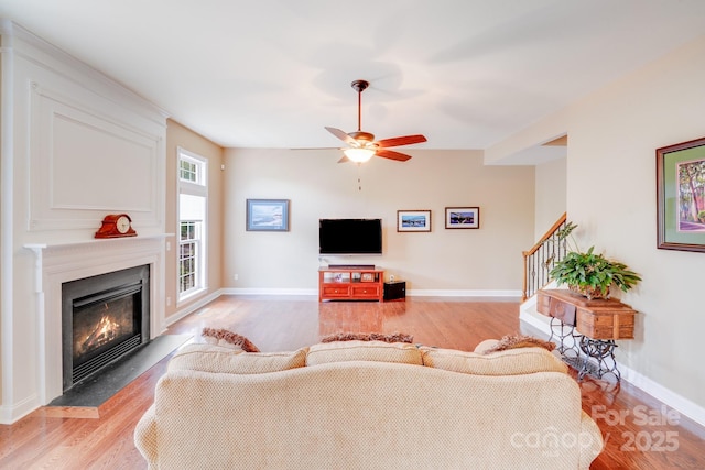 living room with light wood-style floors, ceiling fan, stairway, and a glass covered fireplace